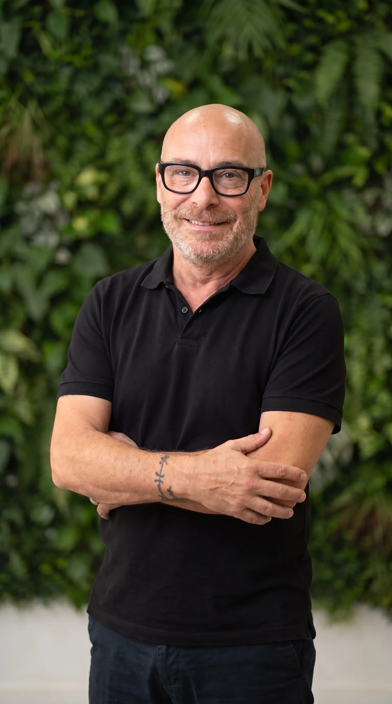 Francesc Peytavi de pie ante el muro vegetal del salón, cabeza rapada, gafas negras y barba canosa, sonriendo con los brazos cruzados